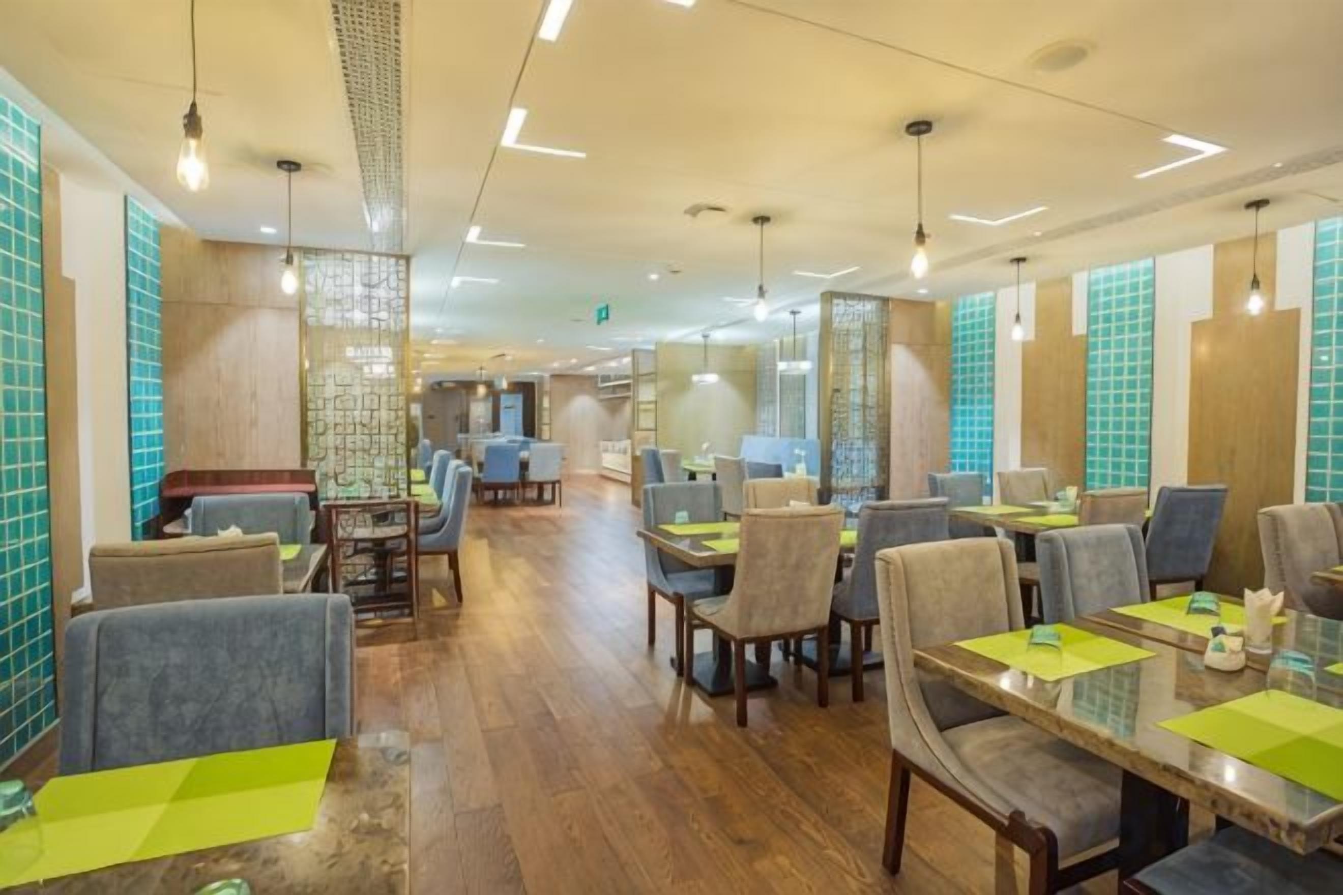 Een restaurant met meerdere tafels en stoelen, houten vloeren en hangende lampen.