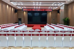 A conference room with rows of white chairs, a stage with a red carpet, and a large screen. - Chengtou Gangwan Hotel (Zunyi)