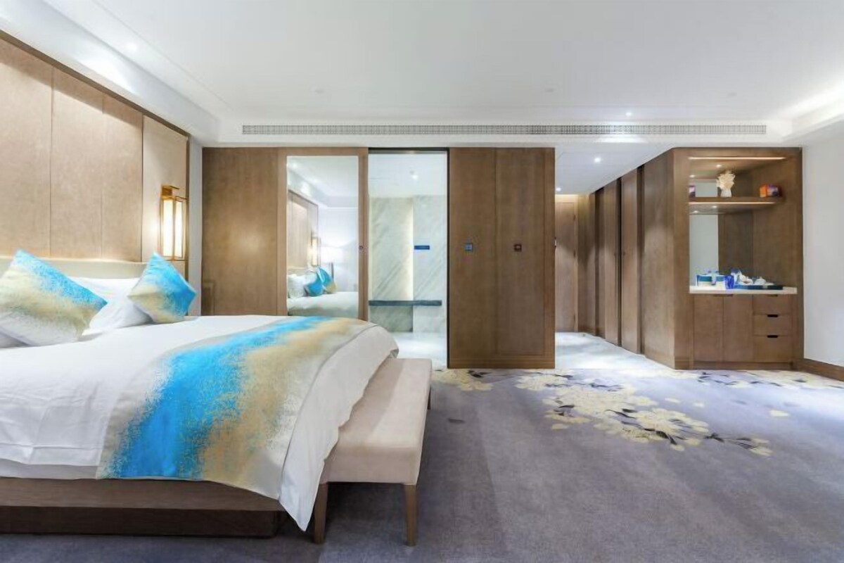 A modern hotel room with a large bed, a walk-in closet, and a bathroom with a mirror and shelves.