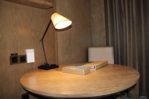 Uma mesa de madeira redonda com uma luminária, uma cadeira e um livro.