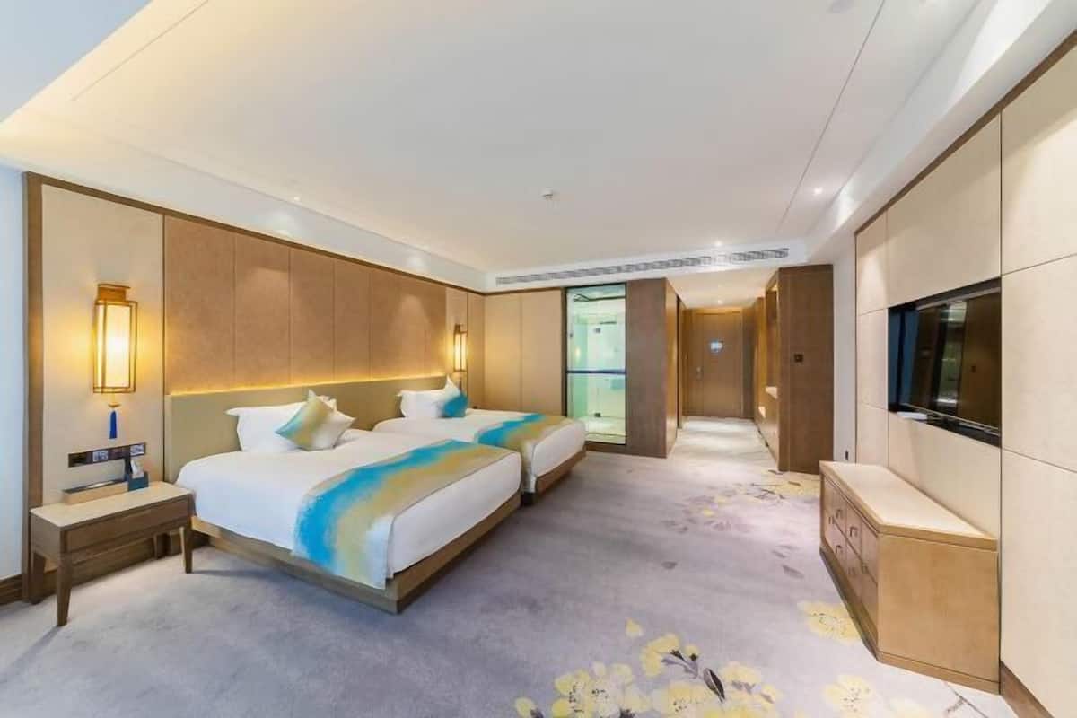 Ein Hotelzimmer mit zwei Betten, einem Fernseher, einem Schreibtisch und einem begehbaren Kleiderschrank.