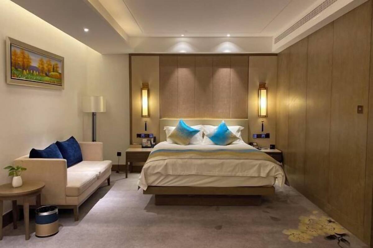 Ein Hotelzimmer mit Bett, Sofa, Nachttisch, Lampe und einem Bild an der Wand.