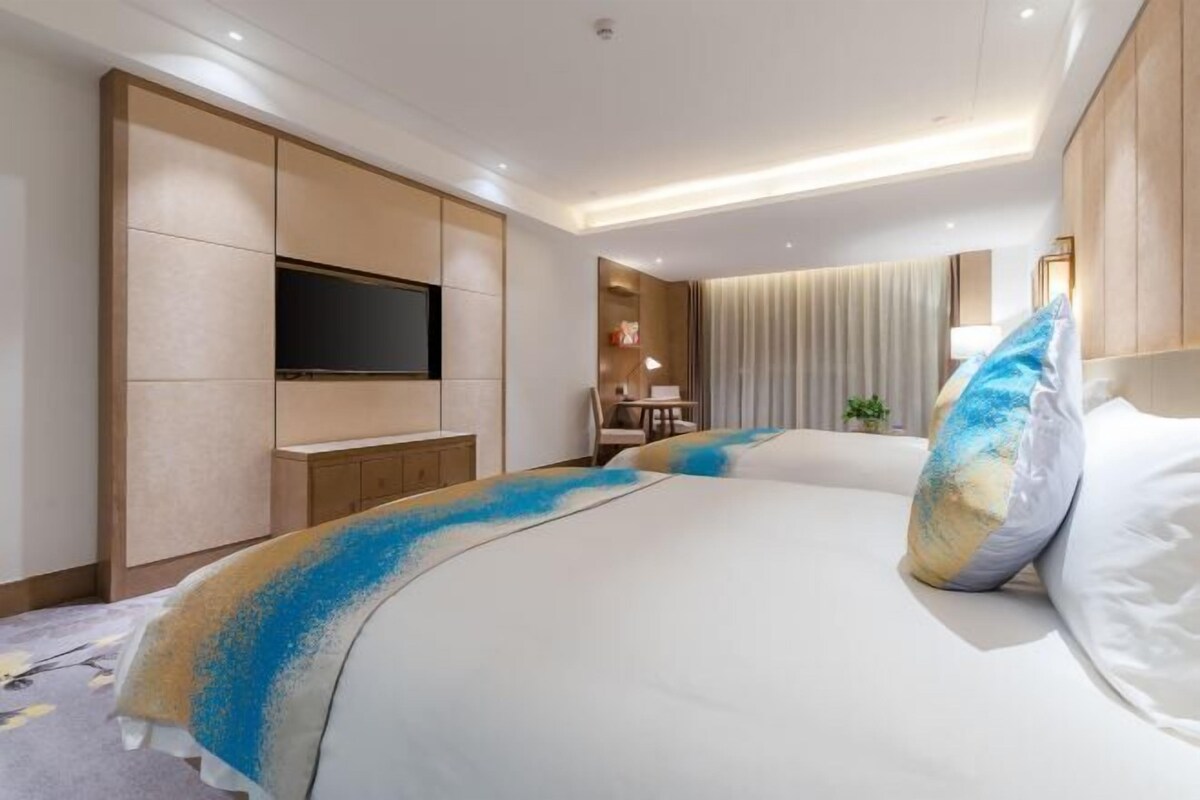 A hotel room with a large bed, a flat-screen TV mounted on the wall, a desk, and a chair.