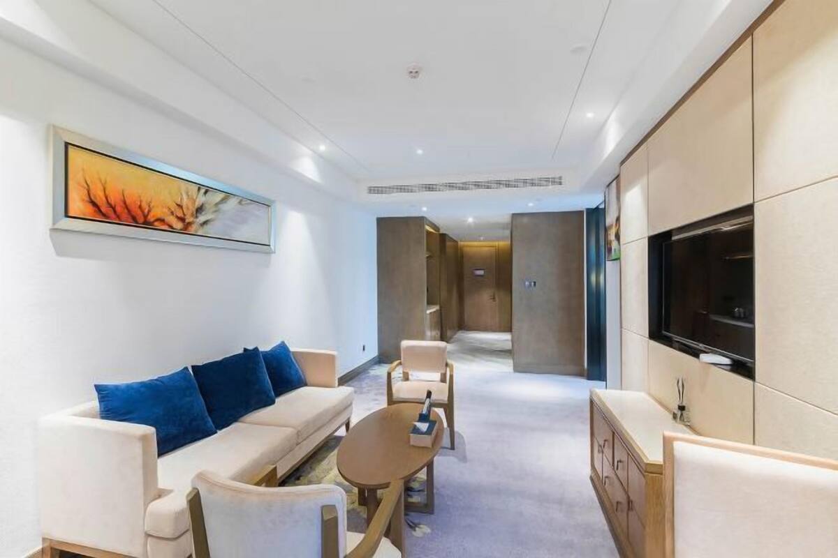 Ein modernes Hotelzimmer mit einer Couch, Sesseln, einem Couchtisch, einem Fernseher und einem Bild an der Wand.