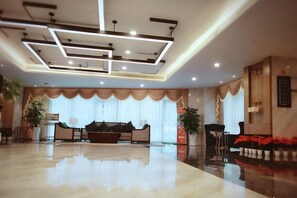 A spacious lobby with a high ceiling, a seating area with a sofa and chairs, and a large window with curtains. - Chengtou Gangwan Hotel (Zunyi)