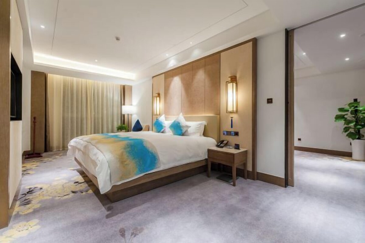 A hotel room with a large bed, bedside tables, a lamp, and a potted plant.