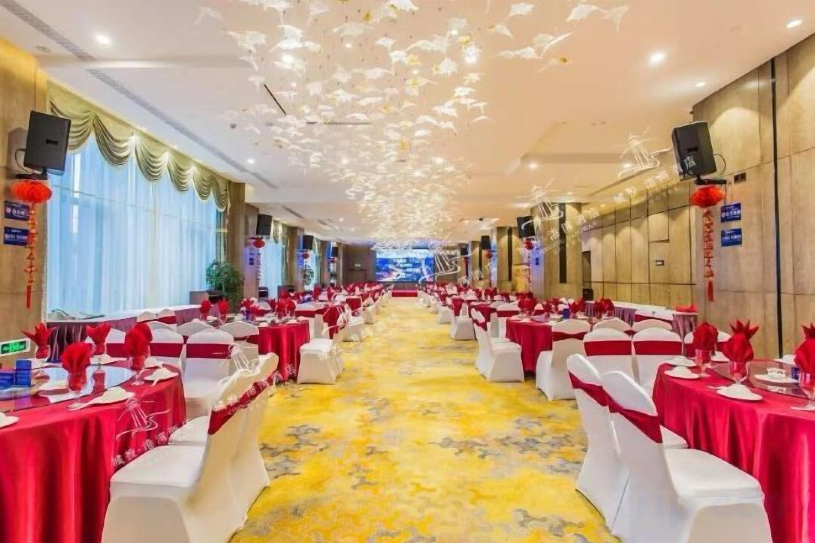 Un salón de banquetes con filas de mesas, sillas blancas y manteles rojos.