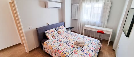 A bedroom with a bed, a desk, a chair, a ceiling fan, and a window with curtains.