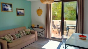 A living room with a sofa, a table, and a view of the outdoors through a sliding door. - T2 quiet, swimming pool, beach 400 m, terrace not overlooked (Six-Fours-les-Plages)