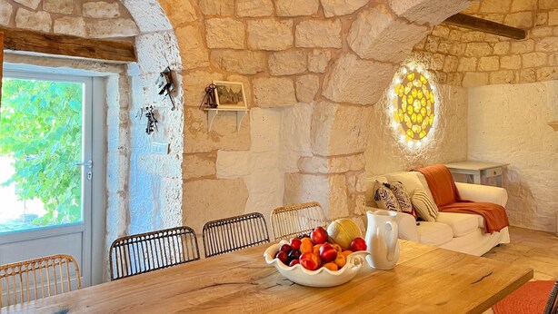 A rustic stone interior with a wooden dining table, white sofa, and a bowl of fruit. - TD Trulli Locobello Stylish Cozy Trulli w Pool (Martina Franca)