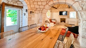 A rustic stone-walled room with a wooden dining table, chairs, and a fruit bowl. - TD Trulli Locobello Stylish Cozy Trulli w Pool (Martina Franca)