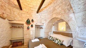 A bedroom with stone walls, a bed with a green bedspread, white pillows, and a nightstand. - TD Trulli Locobello Stylish Cozy Trulli w Pool (Martina Franca)