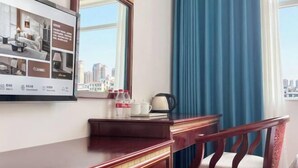 A hotel room with a wooden desk, a chair, a large mirror, and a window with blue curtains. - Beiliu Grand Hotel (Guijiang Pearl Pedestrian Street) (Beiliu)