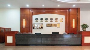 A reception desk with a wooden panel design, a wall-mounted clock, framed certificates, and a potted plant. - Beiliu Grand Hotel (Guijiang Pearl Pedestrian Street) (Beiliu)