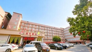 A multi-story hotel with a parking lot, several cars, and a tree with red flowers. - Beiliu Grand Hotel (Guijiang Pearl Pedestrian Street) (Beiliu)