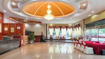 A hotel lobby with a reception desk, a staircase, and a seating area with tables.