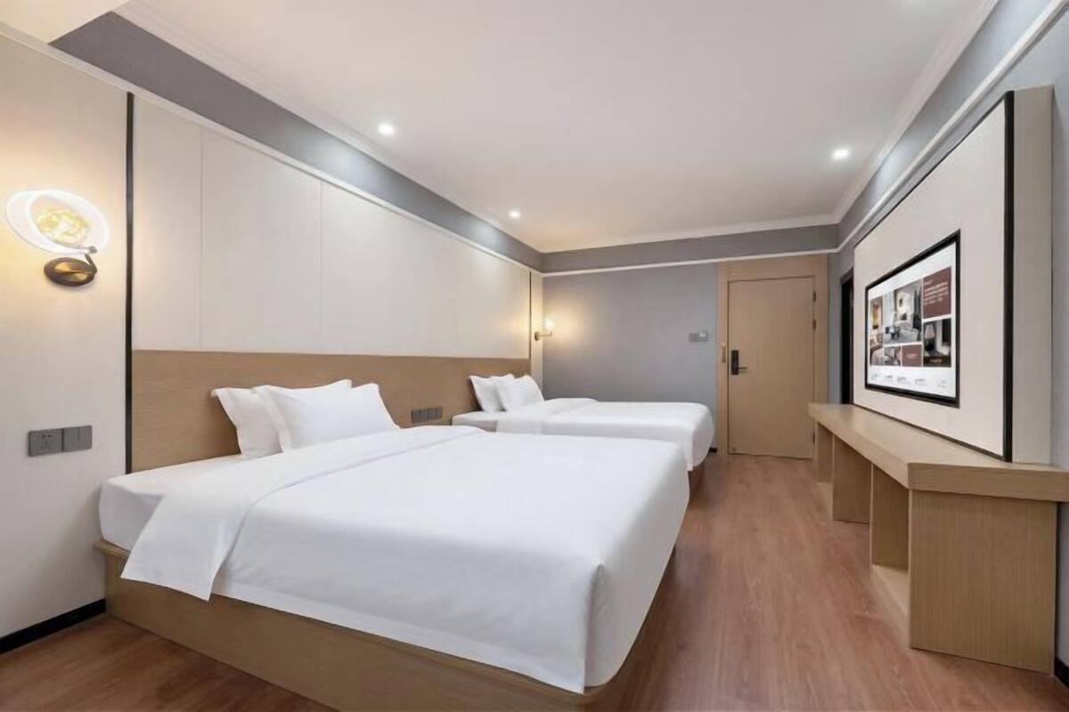 A hotel room with two beds, a bedside table, a wall-mounted light, and a framed picture on the wall.