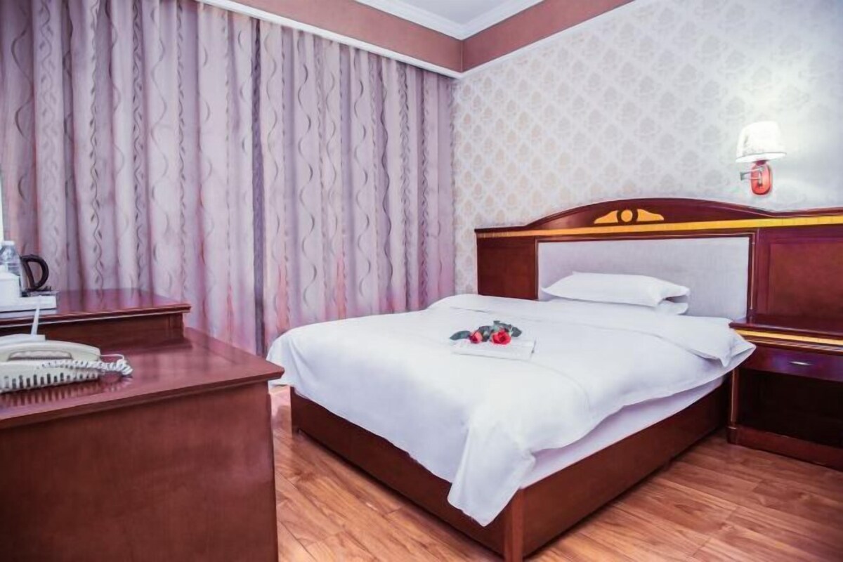 Habitación de hotel impecable con una cama de madera, una mesita de noche, un escritorio con teléfono y una lámpara en la pared.