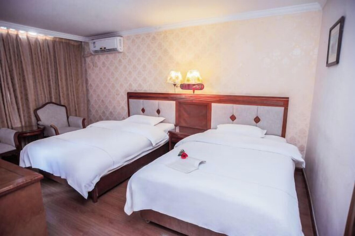 Habitación de hotel con dos camas, un escritorio, una silla y aire acondicionado instalado en la pared.