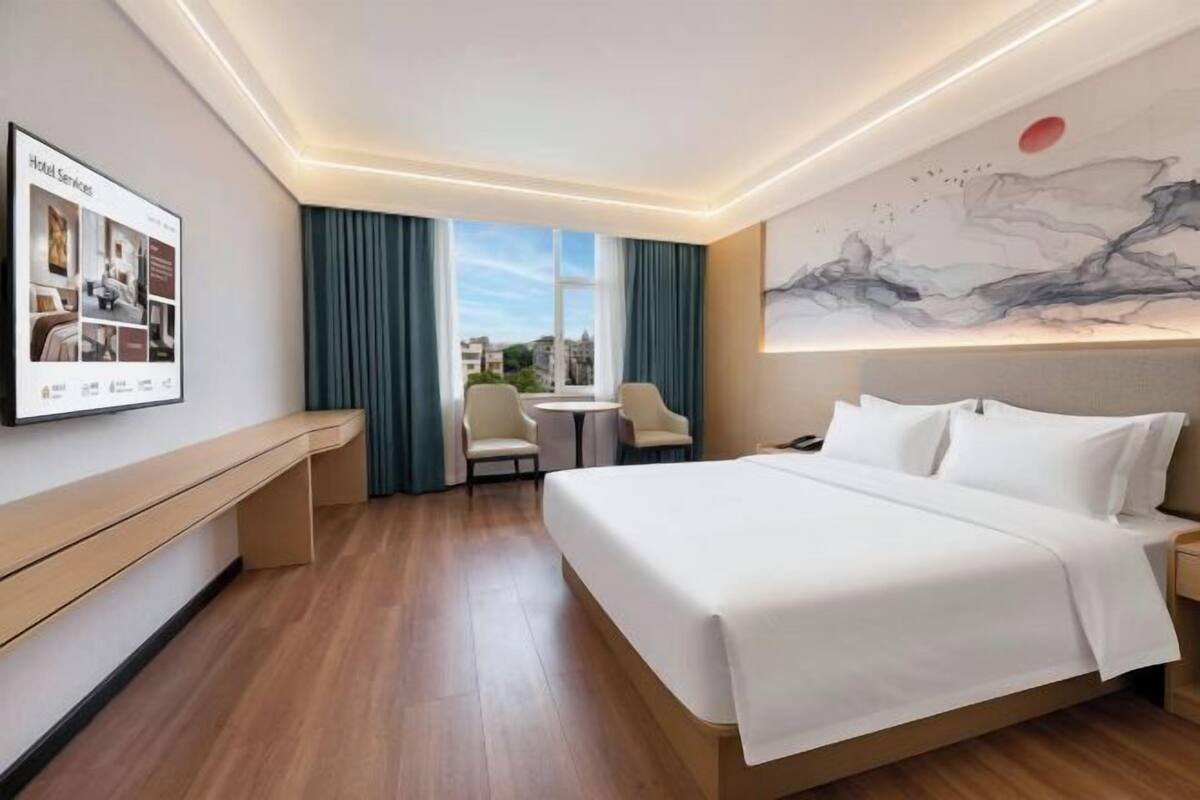 A hotel room with a bed, a desk, a chair, a small table, and a painting on the wall.