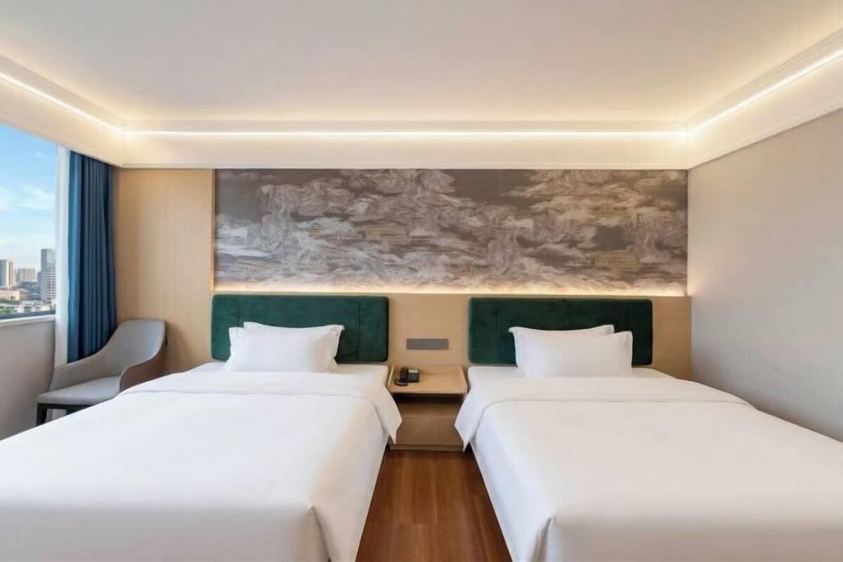 A hotel room with two beds, a city view, a large abstract painting on the wall, and a modern design.