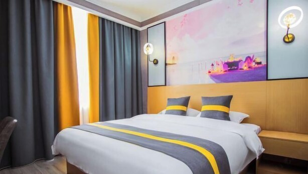 A hotel room with a large bed, a bedside table, a chair, and a wall with a cityscape painting. - Beiliu Grand Hotel (Guijiang Pearl Pedestrian Street) (Beiliu)