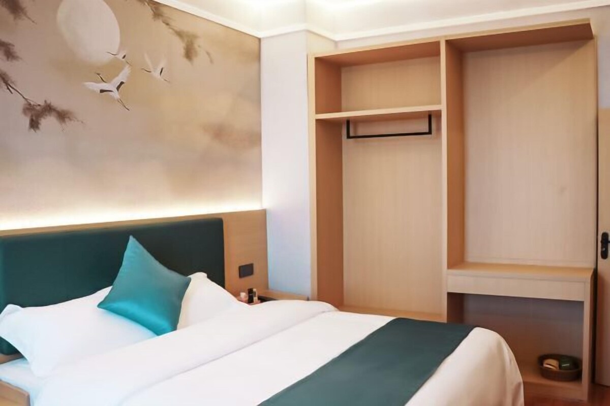 Una habitación de hotel con una cama, una mesita de noche, un estante en la pared y un armario.