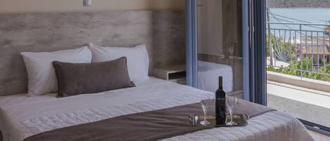 A bedroom with a large bed, a glass door leading to a balcony, and a view of the sea.