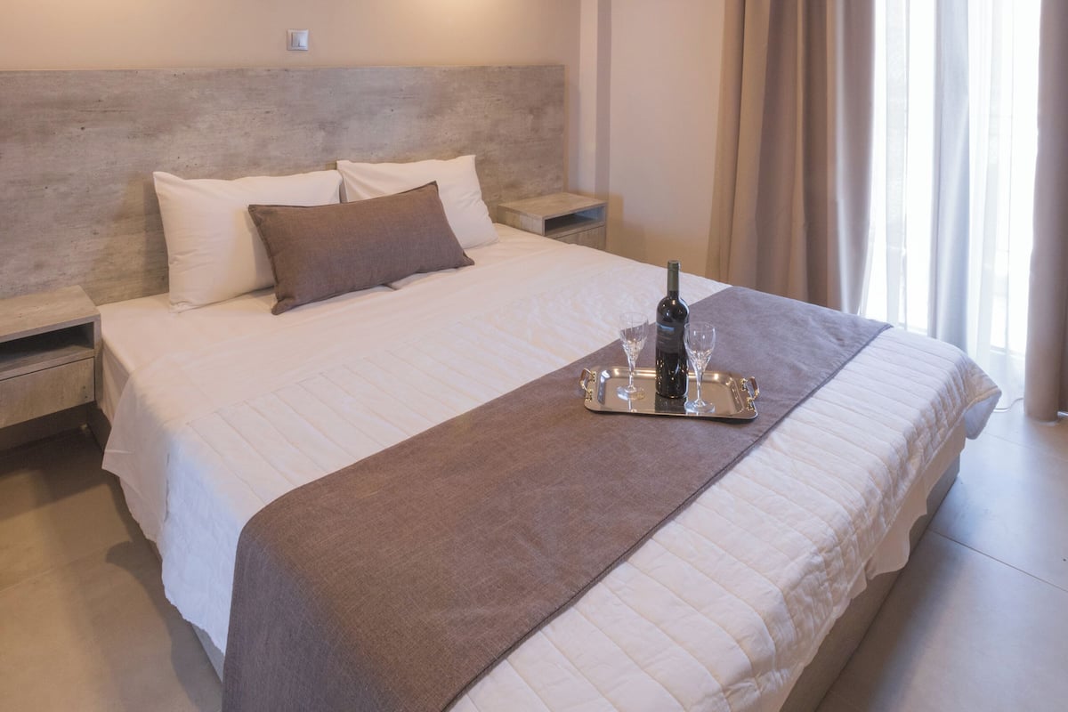 A neatly made bed with a tray of wine glasses and a bottle, a headboard, and two pendant lights.
