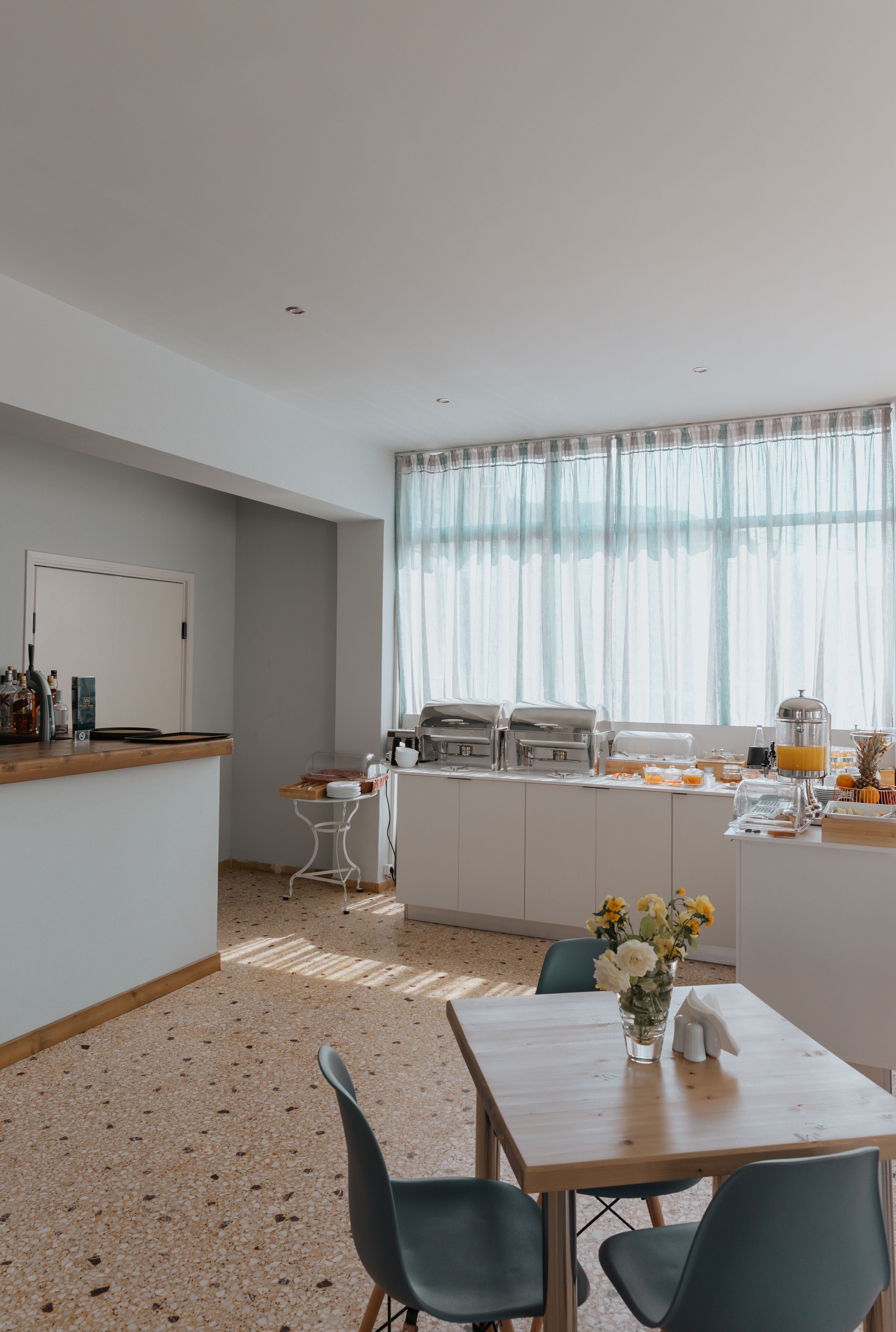 A modern kitchen with a breakfast bar, white cabinets, and a large window with sheer curtains.