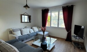 Una sala de estar con sofá, una mesa de centro, un mueble para la televisión y una ventana con cortinas.