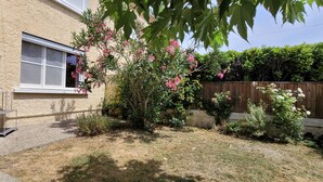 Een huis met een raam, een kleine tuin met verschillende planten en een houten omheining.