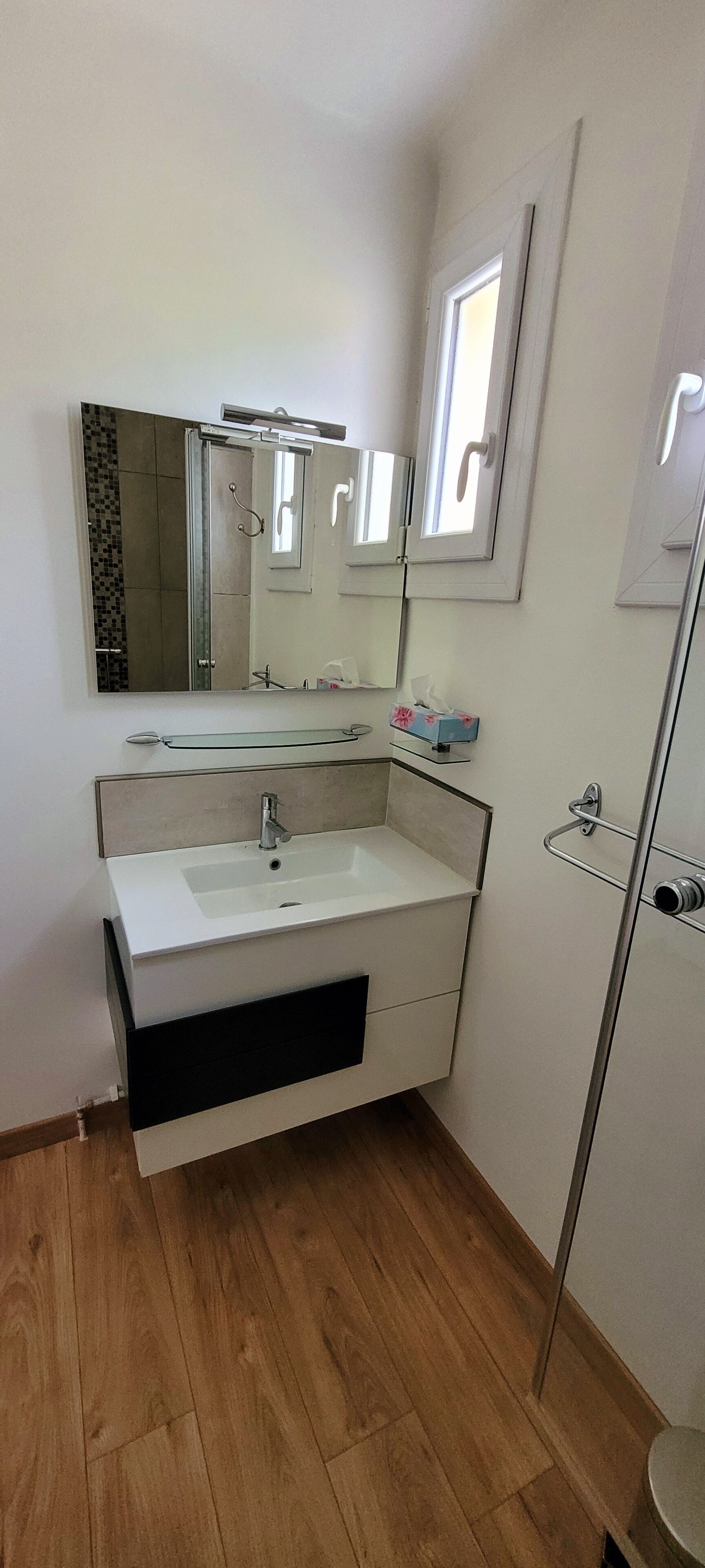 Une salle de bain moderne avec un lavabo blanc, un grand miroir et une douche à parois de verre.