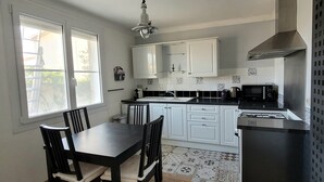 Een keuken met witte kastjes, een zwart aanrecht, een eettafel met stoelen, een raam en een magnetron.