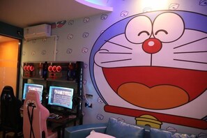 Ein Zimmer mit einer großen Wandmalerei eines Comic-Charakters, Gaming-Stühlen, zwei Monitoren und einer Decken-Klimaanlage.