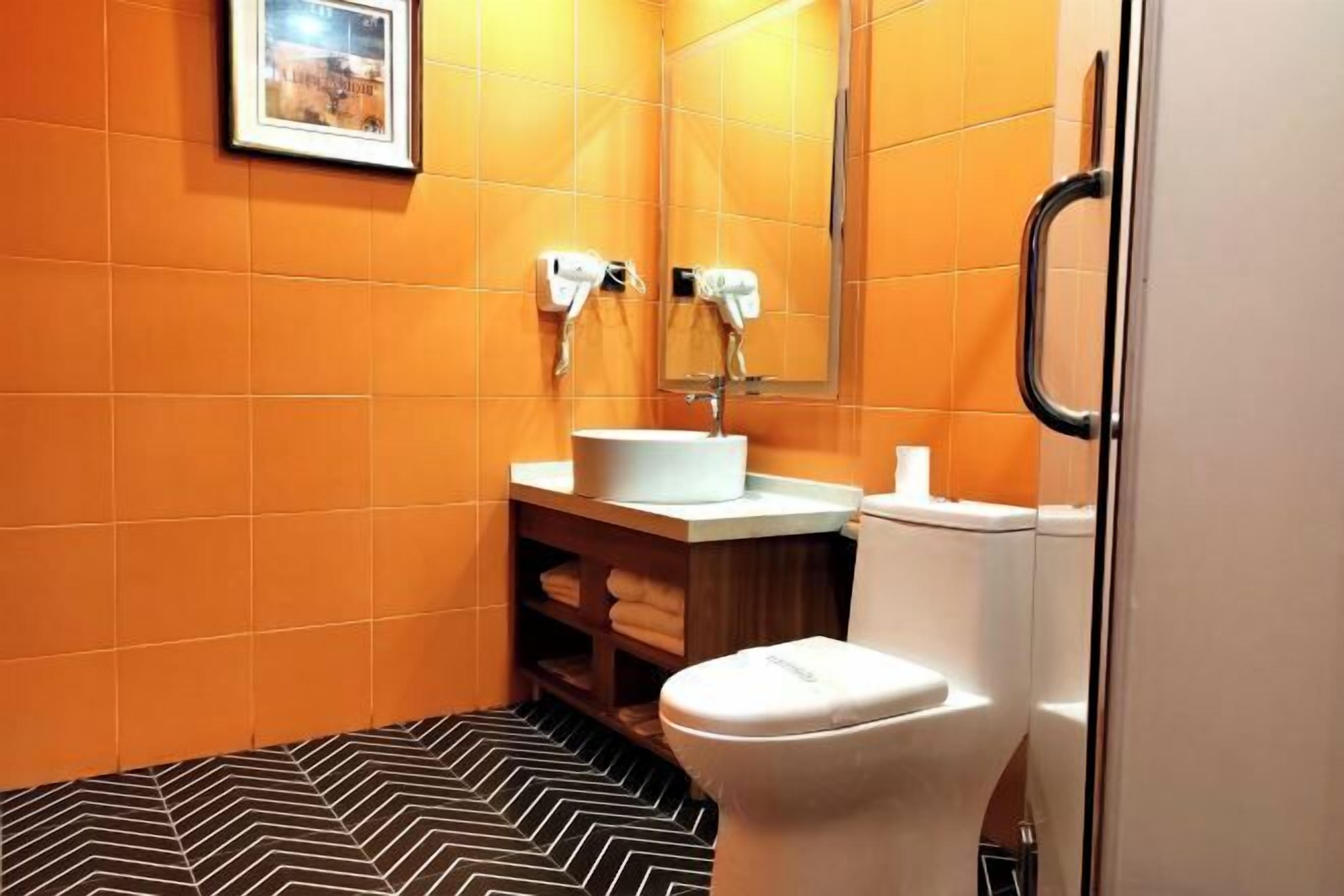 A bathroom with orange tiles, a white sink, a mirror, and a toilet.