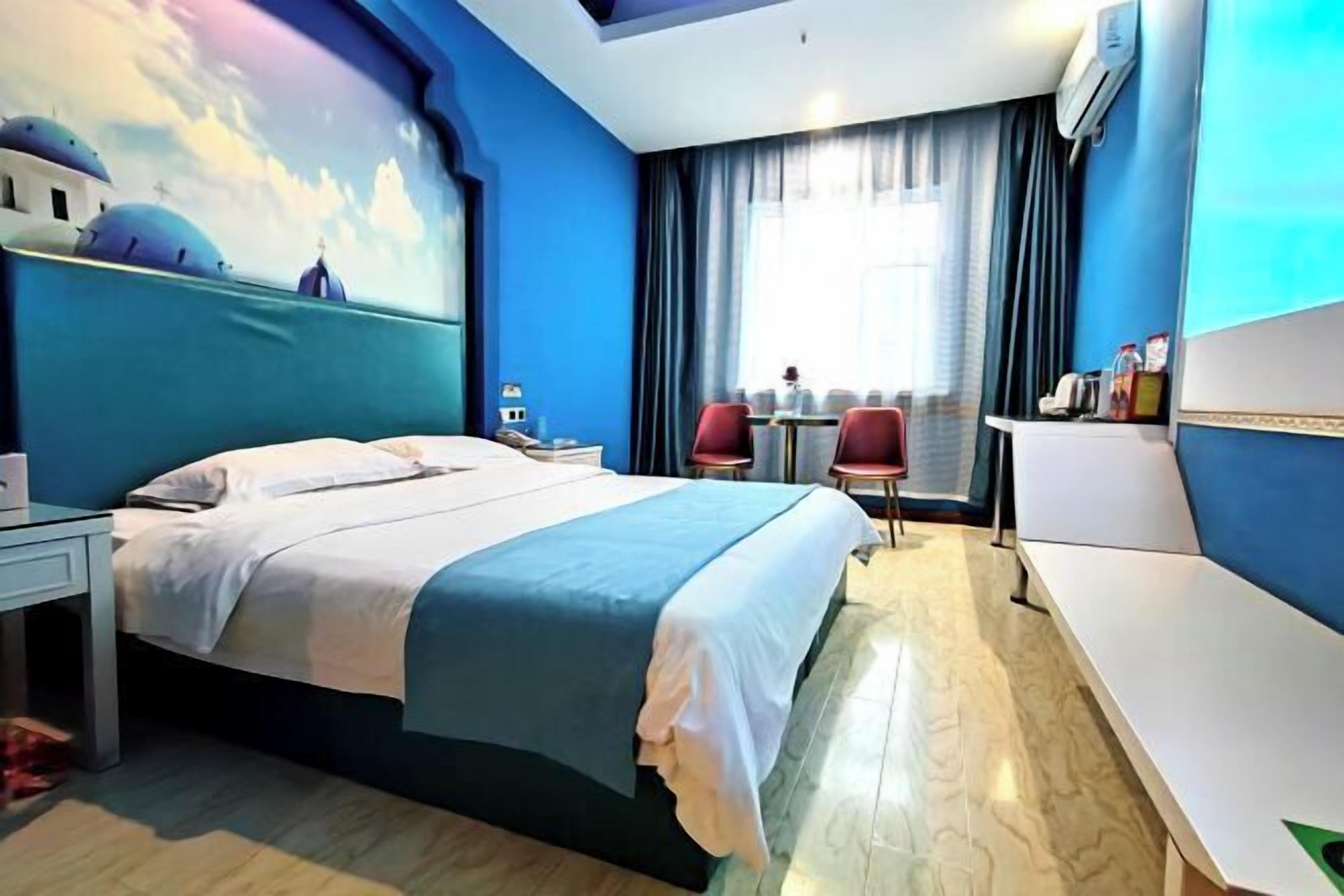 Habitación de hotel con cama, escritorio, silla, una mesita y ventana con cortinas.