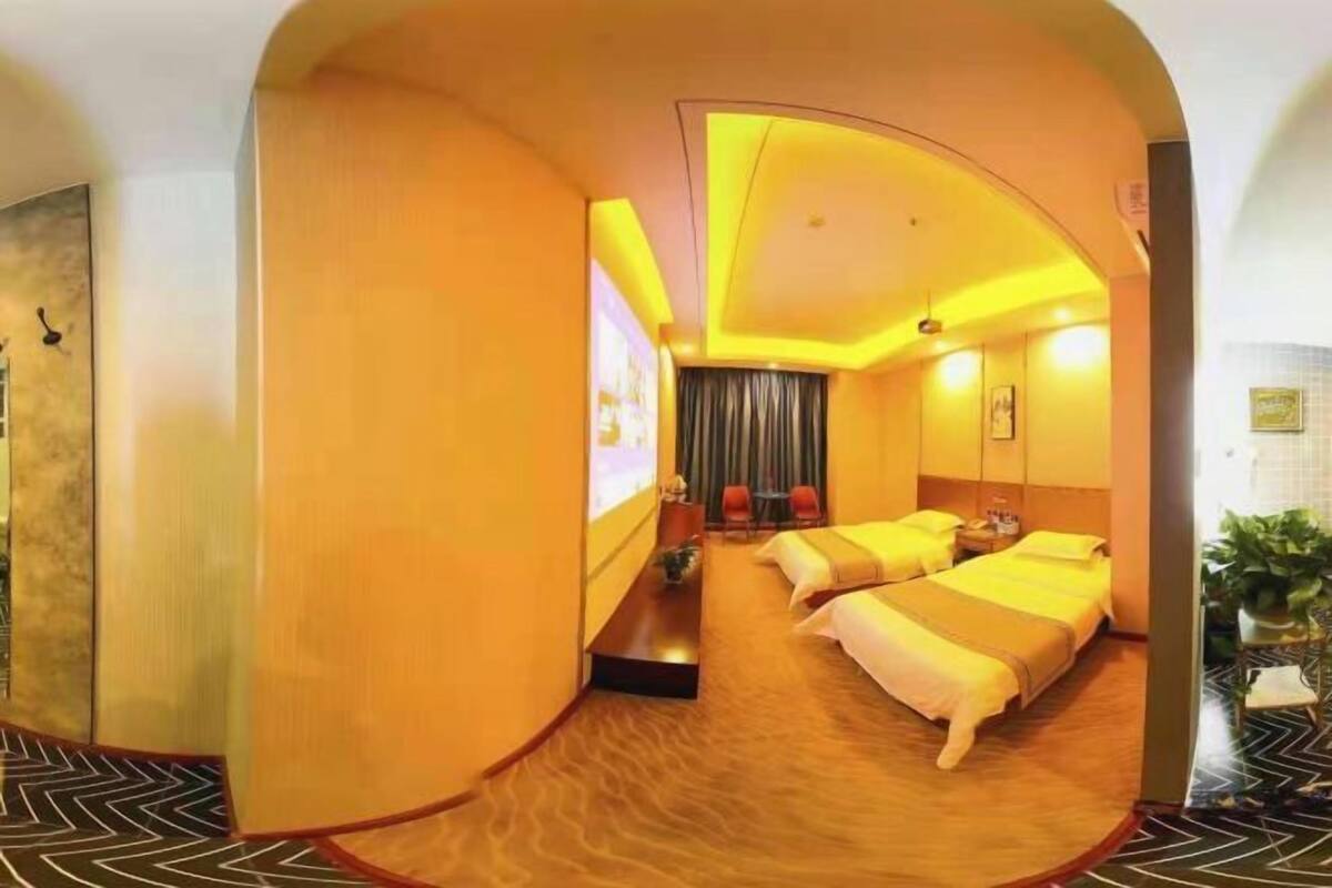 Hotellihuone, jossa on kaksi sänkyä, oleskelualue tuoleineen, televisio ja huonekasvi.