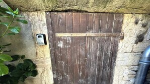 A rustic wooden door with a metal latch, set against a textured stone wall. - Nid douillet - Centre historique (Buxy)