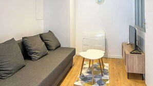 A modern living room with a grey sofa, a small white table, a TV on a wooden stand, and decorative wall art. - Nid douillet - Centre historique (Buxy)