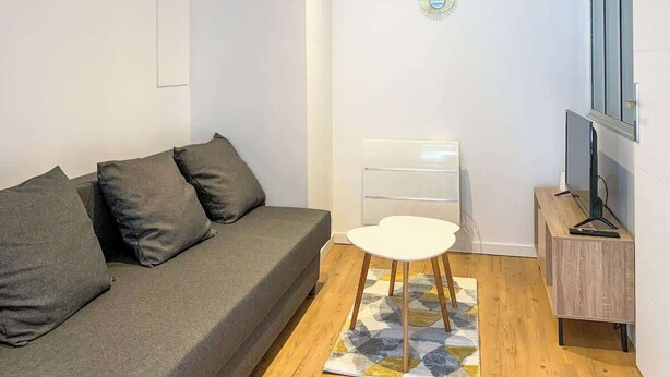 Un salon moderne avec un canapé gris, une petite table blanche, un téléviseur posé sur un meuble en bois et des œuvres d’art décoratives accrochées au mur.