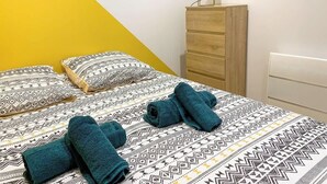 Un lit avec une literie à motifs, une commode en bois et une lampe.