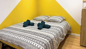 A bed with patterned bedding and rolled towels, a wooden wardrobe, and a mirror on the wall. - Nid douillet - Centre historique (Buxy)