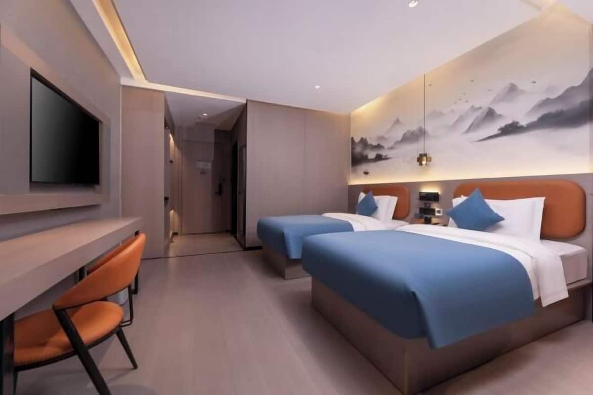 A hotel room with two beds, a desk, and a TV.