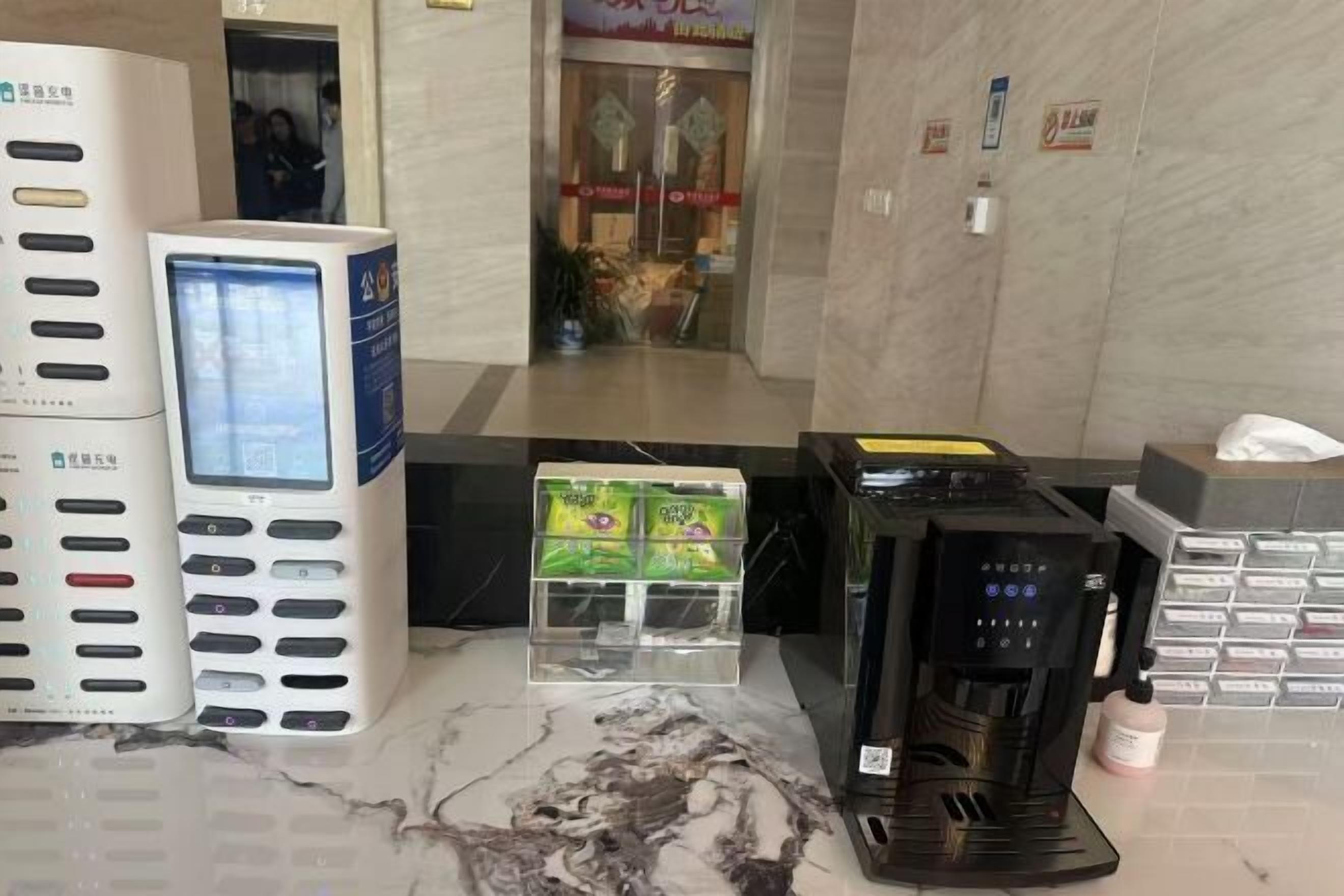 Una recepción con mostrador, una pantalla digital, una cafetera y una máquina expendedora.