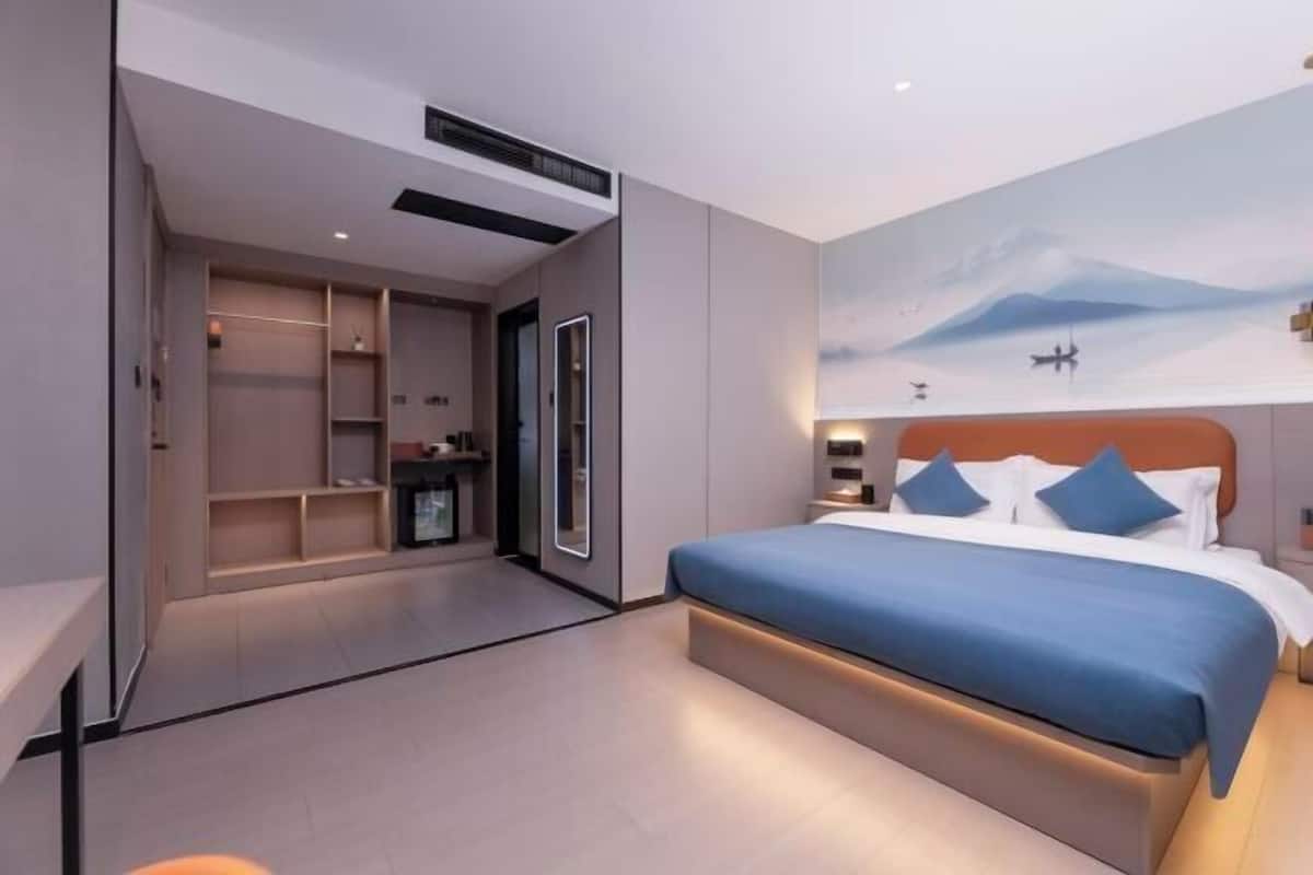A modern hotel room with a large bed, built-in wardrobe, and a scenic wall mural.
