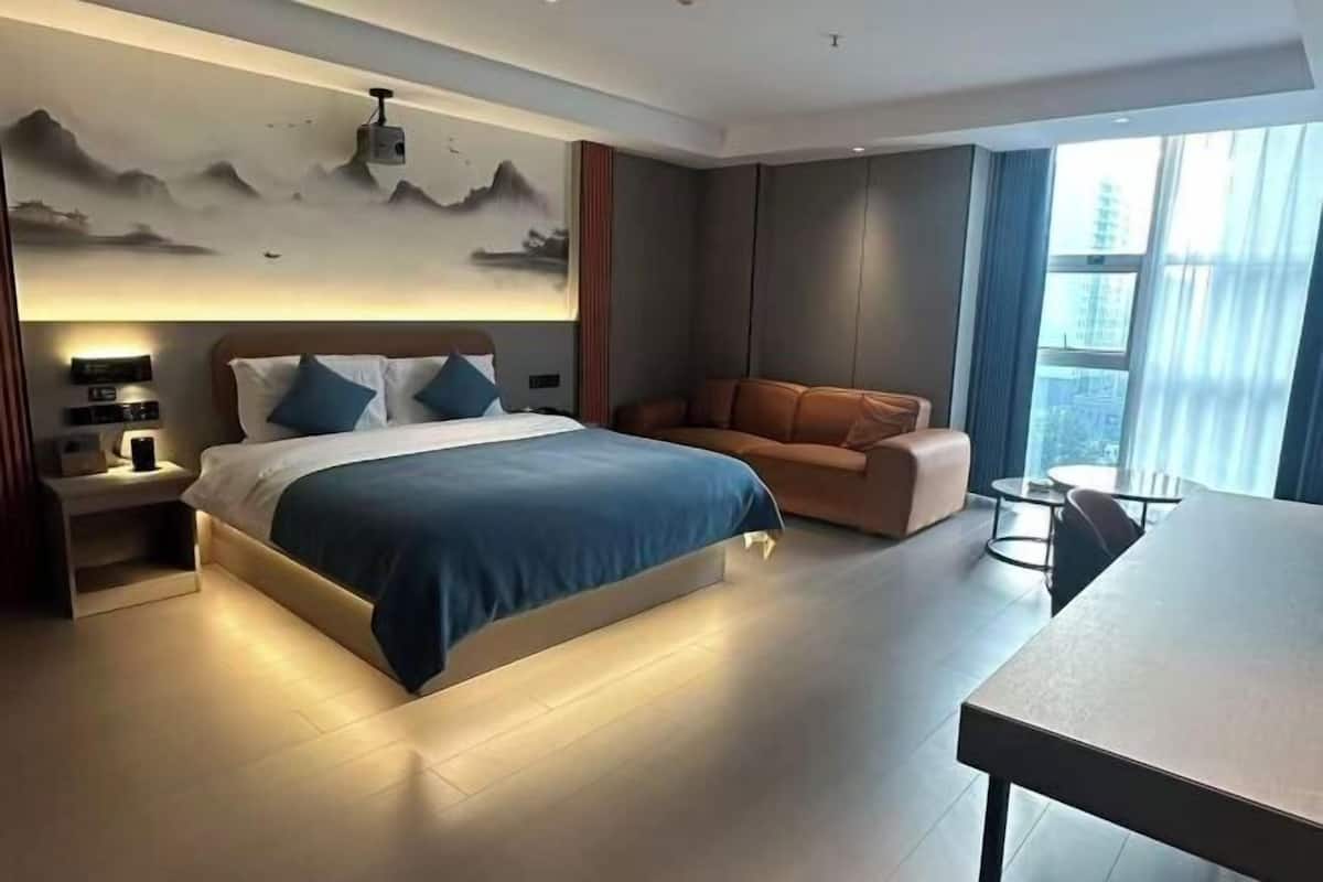 A modern bedroom with a large bed, a sofa, a small table, and a wall-mounted projector.