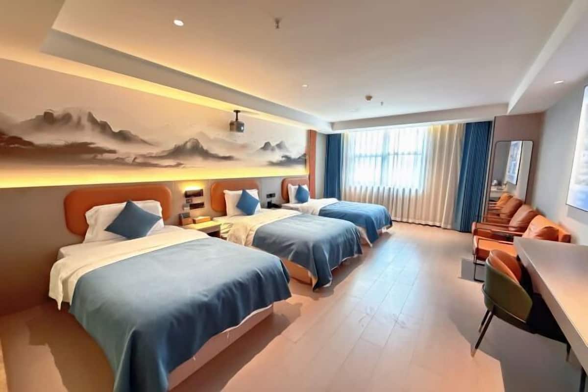 A hotel room with three beds, a sofa, a desk, and a large window with curtains.
