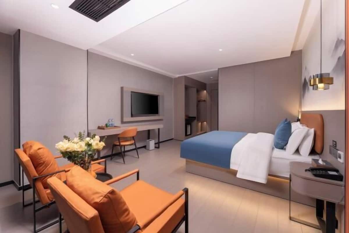 A modern hotel room with a bed, a desk, a chair, and a TV.