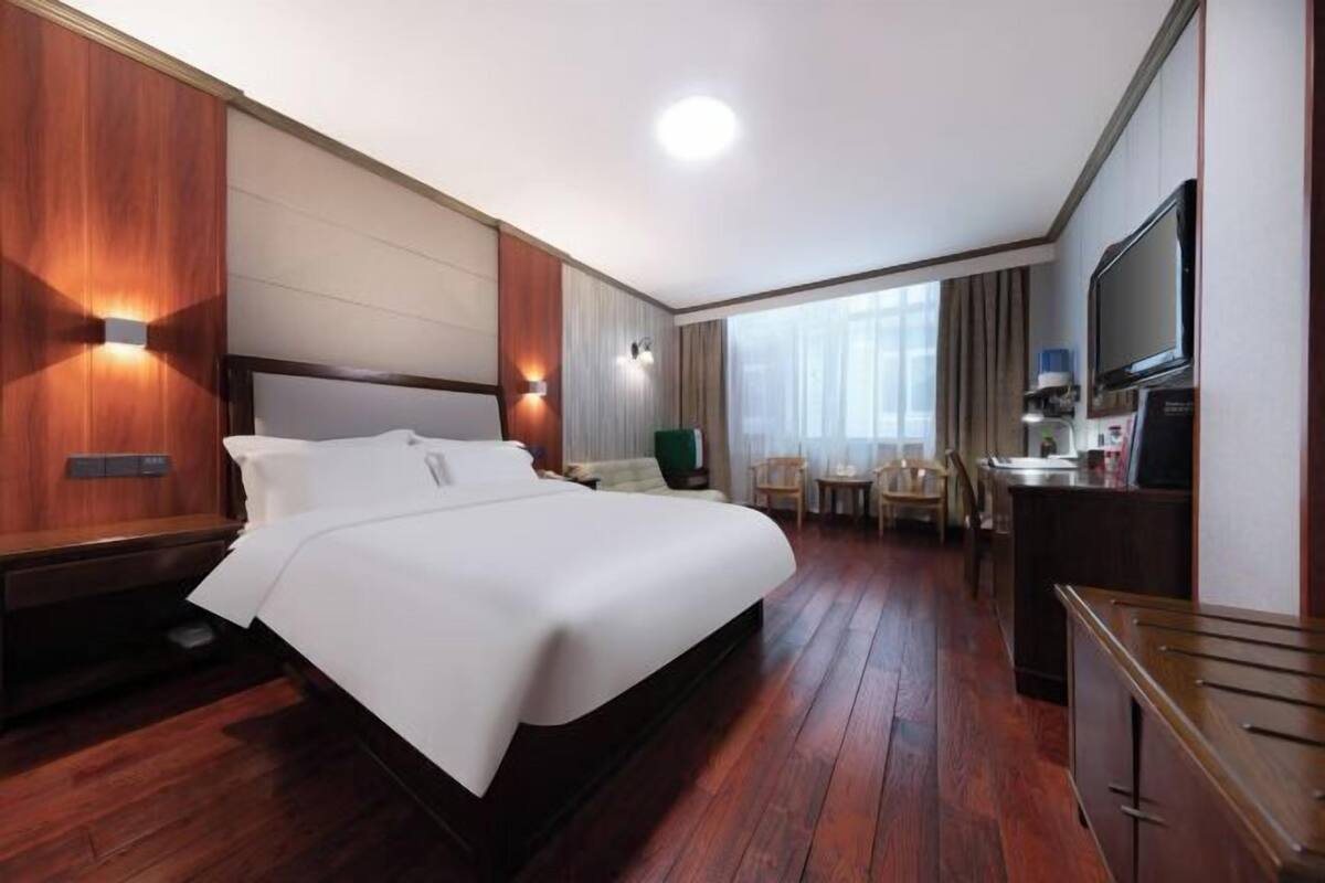 Una habitación de hotel con una cama grande, un escritorio con silla, un televisor y una ventana con cortinas.